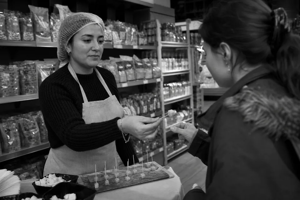 Hostessa podaje klientce porcję do spróbowania przy stoliku degustacyjnym w alejce supermarketu