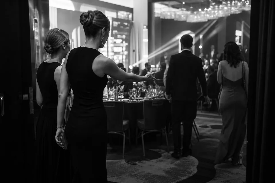 Hostessy prowadzą gości do stołów na gali firmowej w sali balowej hotelu